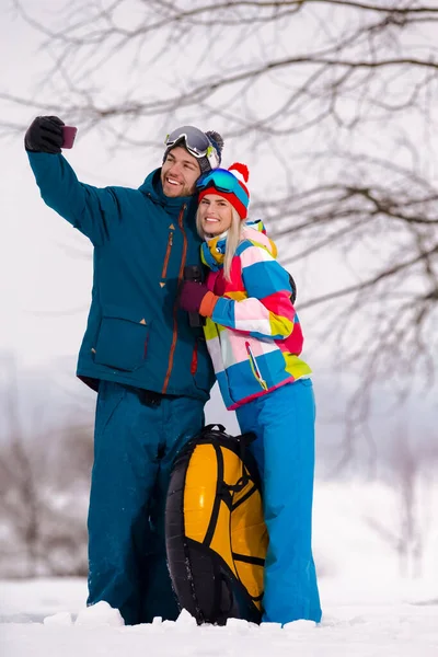 Smiling  Caucasian Couple With Snow Tubes Taking Selfie Pictures During Winter Activities in Mountains. Vertical Image