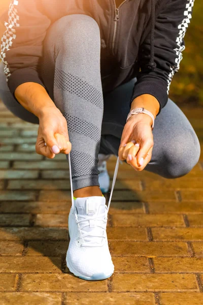 Outdoor Sport Concepts. Active Female Runner Tighten Up Her Shoelaces During Jogging Training Exercise Outdoor. Vertical Image