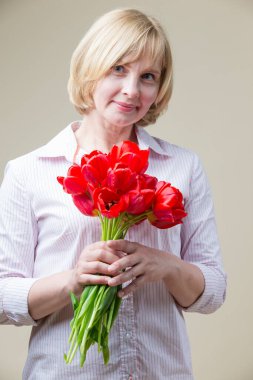 Beyaz, bej arka plana karşı bir sürü güzel kırmızı lalesi olan yaşlı bir kadın. Dikey Resim