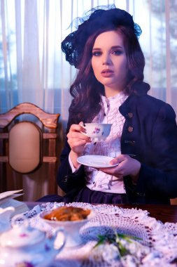 Kafkasyalı esmer kadın portresi. Evde masa başında kitap okurken elinde çay fincanıyla Retro Style pozlar veriyor. Dikey Resim Kompozisyonu