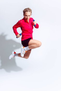 Kırmızı uzun kollu beyaz kadın ve beyaz halterli koşu kıyafetleriyle atlayan. Dikey Çekim