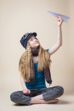 Uçan Gear 'da Uçan Kafkasyalı Genç Kız Origami Kağıt Uçakla Oturuyor ve Bej Arkaplanda Gülümsüyor. Dikey Resim