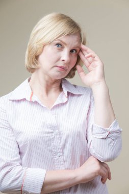 Çekici, olgun, beyaz, bej arka planda el kaldıran yaşlı kadın. Dikey resim kompozisyonu.