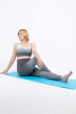 Mavi Mat 'te yoga yapan ve beyaz arka planda spor kıyafetiyle rahatlayan Kafkas bir kadın. Dikey Bileşim