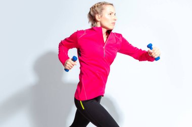 Kırmızı uzun kollu formalı ve beyaz arka planda atlayan koşan etkin halterli bir kadın. Yatay Resim Yönlendirmesi