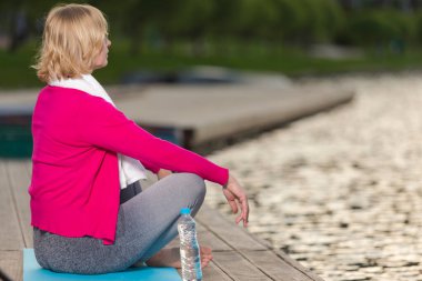 Blue Mat at at Water Shore Outdoor 'da Yoga Uygulaması sırasında Olgun Kafkas Sarışın Kadın portresi. Yatay resim