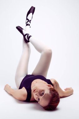 Beyaz kadın dansçı, yerde yatıp bacak bacak bacak bacak üstüne atmış bir şekilde kameraya doğru bakıyor. Dikey Resim Yönlendirmesi
