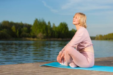 Son sınıf Yoga Fikirleri. Spor Giysileri Giyen Kafkas Kadın, Tahta Sahnede, Su kenarında Yoga Yapıyor. Yatay Resim Kompozisyonu