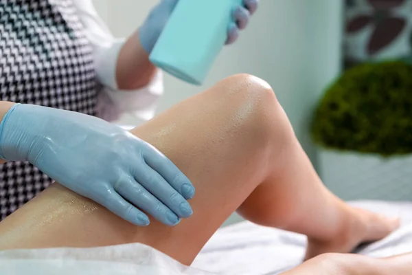 Beautician During Wax Depilation Procedure of Legs By Wax Device on Female Legs in Beauty Salon. Horizontal Image Orientation
