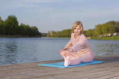 Yoga Bacakları Esneme Eğitimi Sırasındaki Yaşlı Kafkasyalı Kadın Tahta Sahne Sahnesi Açık Deniz kenarında. Yatay Resim Kompozisyonu