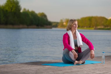 Blue Mat at at Water Shore Outdoor 'da yoga yaparken olgun beyaz kadın. Yatay resim