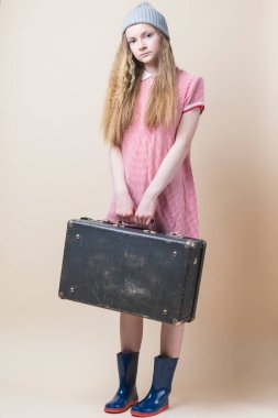 Kırmızı Giysili Sarışın Genç Kız portresi ve Kışlık Şapkalı Lastik Çizmeler Bej Arkaplan Üzerinde Eski Seyahat Bavulu. Dikey Resim