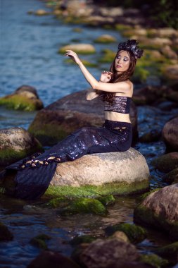 Deniz kızı Kayaların Üzerinde Okyanus Kıyısı Poz Verirken Deniz Kabuğu Süslemeli Taç ve Baştan Çıkarıcı Vücut Üzerinde Siyah Parlak Kuyruk Üstü Üstü Üstü Kalın Kalın Deniz Kraliçesi rolünde.