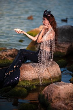 Deniz kabuğu ve deniz kıyısındaki kayalıklarda ağı olan Asyalı deniz kızı. Deniz kabuğu süslenmiş taç ve denizin kraliçesi olarak sarkık vücutlu siyah parlak kuyruk takıyor. Dikey Resim Kompozisyonu