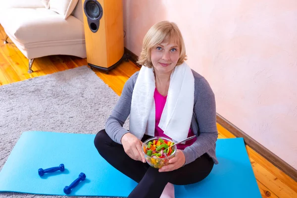 Close-up Portrait of Mature Woman Having Break During Home Exercises Holding Glass Bowl Of Fresh Vegetables. Vertical Image