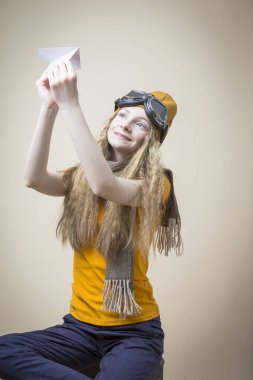 Uçan Dişliler ve Sıcak Şapkalı Beyaz Kız, Origami Kağıt Uçağı 'nı Bej Arkaplan Üzerinde Fırlatıyor. Dikey Kompozisyon