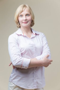 Gülümseyen Kafkasyalı Olgun Kadın 'ın portresi. Bej arka planda katlanmış elleri ile dimdik duruyor. Dikey Resim