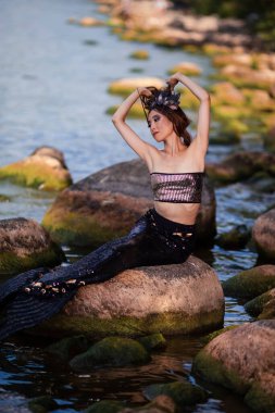 Deniz kızı Okyanus Kıyısındaki Kayalıklarda Pozlar Deniz kabuğu tacı takıyor ve baştan çıkarıcı vücuda siyah parlak kuyruk takıyor ve Denizin Muhteşem Kraliçesi rolünde Strass 'larla kaplı. Dikey Bileşim