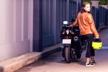 Kaskı elinde tutarken spor motosikletine yaslanan Kafkasyalı genç bir motorcu. Yatay Bileşim