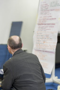 Önünde uzun kağıt sunu Sh oturan erkek öğretim görevlisi