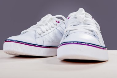 Pair of White Fashionable Leather Trainers on Wooden Surface Against Gray Background.
