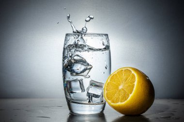 Bir bardak su, limon ve buz. Su sıçraması, bir bardak suda fırtına. Yuvarlak monokrom gradyan arkaplan.