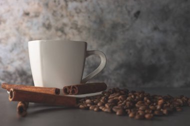 Beyaz fincan, tarçın ve gri arka planda kahve çekirdekleri. Sabah kahvesi. Kahve dükkanı menüsü.