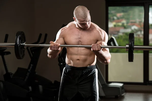 Hombre en el gimnasio ejercitando bíceps con barra — Foto de Stock