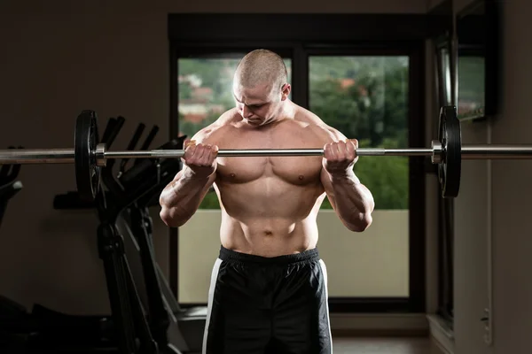 Hombre en el gimnasio ejercitando bíceps con barra — Foto de Stock