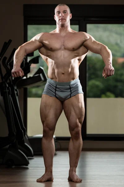 Hombre joven flexionando los músculos en el gimnasio — Foto de Stock