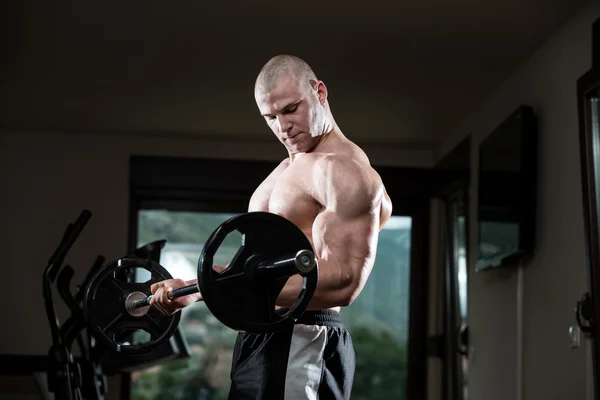 Hombre en el gimnasio ejercitando bíceps con barra — Foto de Stock