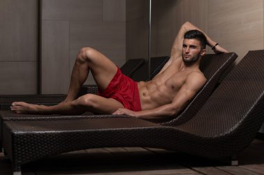 Yüzme havuzunun kenarında şezlong üzerinde oturan adam