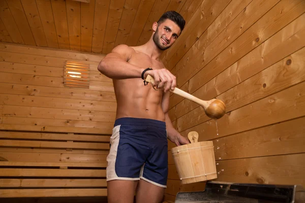 Pohledný muž, nalití vody na horké kameny v sauně — Stock fotografie