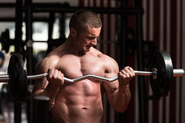 Culturista ejercitando bíceps con barra en el gimnasio —  Fotos de Stock