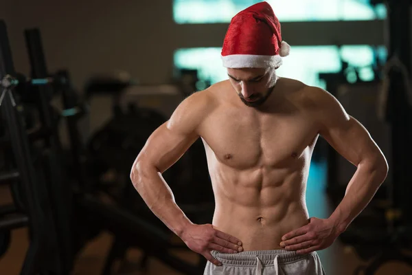 Мускулистый мужчина в шапке Санта Клауса в спортзале — стоковое фото