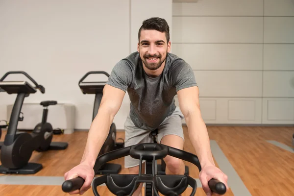 Uomo muscolare che fa ciclismo nel moderno centro fitness — Foto Stock