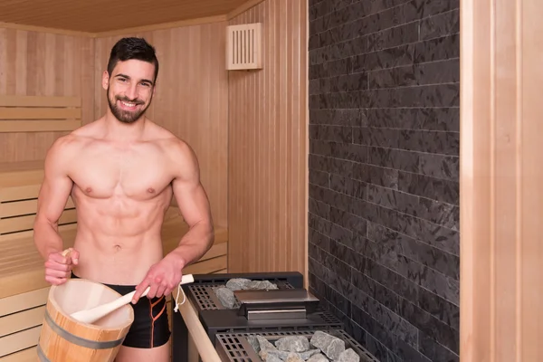 Pohledný muž, nalití vody na horké kameny v sauně — Stock fotografie