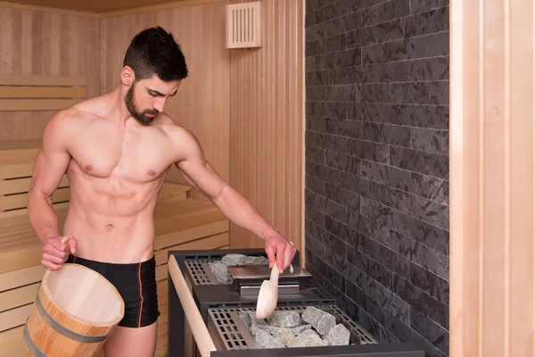 Knappe Man gieten van Water op hete stenen In Sauna — Stockfoto