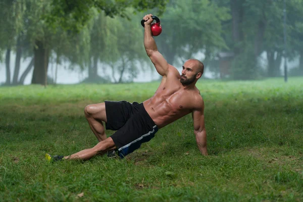Kniender muskulöser Mann, der mit Kettlebells trainiert — Stockfoto