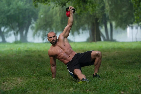 Kniender muskulöser Mann, der mit Kettlebells trainiert — Stockfoto