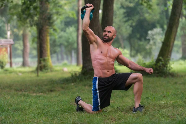 Kniender muskulöser Mann, der mit Kettlebells trainiert — Stockfoto