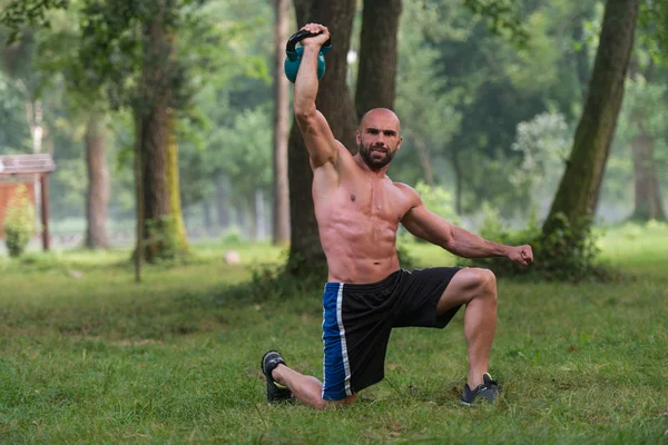 Ajoelhando o homem muscular exercitando com Kettlebells — Fotografia de Stock