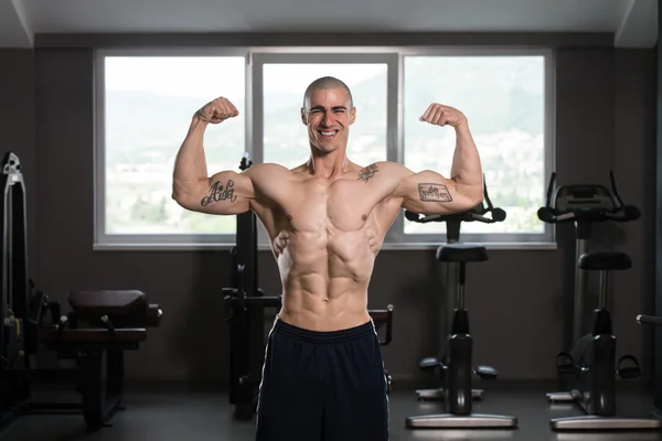 Bicipiti posa di un giovane uomo in palestra — Foto Stock