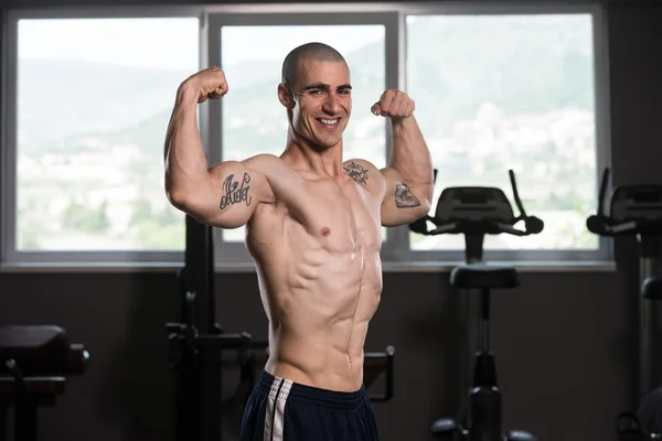 Biceps pose d'un jeune homme dans la salle de gym — Photo