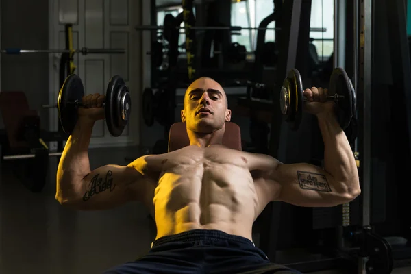 Молодой человек в спортзале упражняется грудь с гантелями — стоковое фото