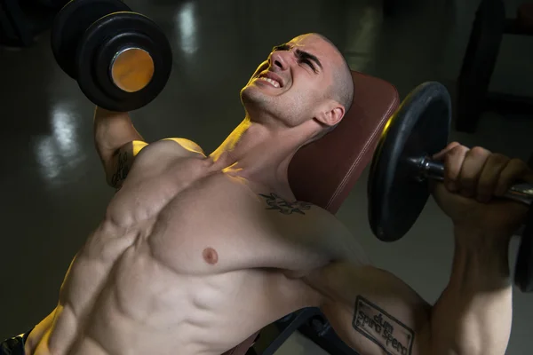 Junger Mann im Fitnessstudio übt Brust mit Hanteln — Stockfoto