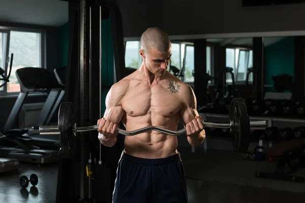 Hombre en el gimnasio ejercitando bíceps con barra — Foto de Stock