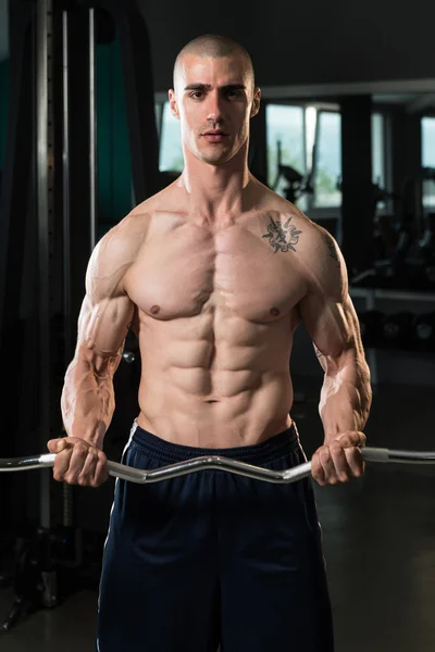 Hombre en el gimnasio ejercitando bíceps con barra —  Fotos de Stock