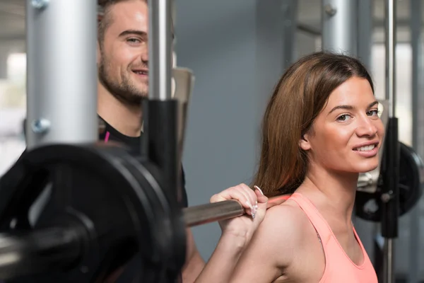 Entrenador de gimnasio ayudando a la mujer en sentadilla Barbell —  Fotos de Stock