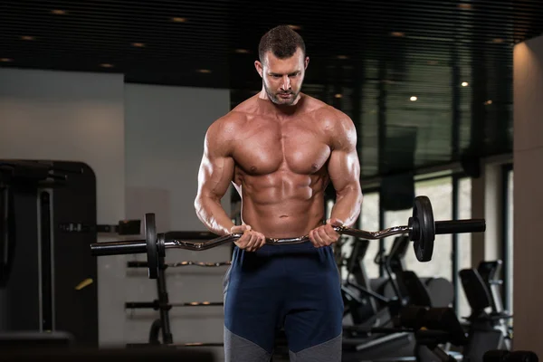 Hombre muscular ejercitando bíceps con barra — Foto de Stock